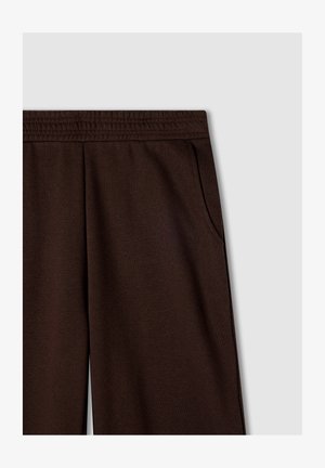 Pantaloni della tuta marroni con vita elasticizzata, tasche laterali e un tessuto morbido e texturizzato. Design semplice, senza motivi o accenti visibili.