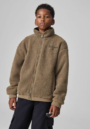 Brun fleecejacka med hög hals, fullständig dragkedja och ribbad nederkant. Har texturerad tyg och broderad logotyp på bröstet.