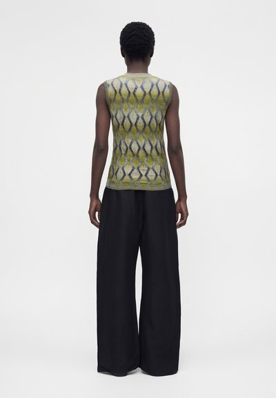 Άτομο που φοράει πράσινο και γκρι μοτίβο τοπ χωρίς μανίκια και φαρδιά μαύρη παντελόνα, σε άσπρο φόντο, βλεπόμενο από πίσω.