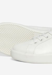 Baskets blanches en cuir lisse, à bout rond, avec des œillets en plastique et une semelle en caoutchouc texturée au motif en chevrons.