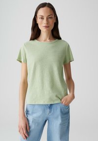 T-shirt verde chiaro a maniche corte, realizzato in tessuto morbido e texturizzato. Collo a giro, vestibilità rilassata, abbinato a jeans denim azzurri.