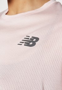 Svetlo roza športna majica, izdelana iz dihljivega, perforiranega materiala. Ima črn logotip spredaj, krožni izrez in kratke rokave.