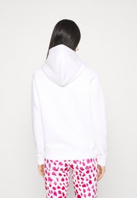 Sudadera blanca con una capucha amplia, textura suave y puños de canalé, combinada con pantalones rosa con un patrón de corazones.
