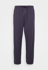 Nike-housut tummansinisinä, valmistettu pehmeästä kankaasta. Ominaisuuksiin kuuluu joustava vyötärö, jossa on nyöri, ja pieni valkoinen logo vasemmalla puolella.