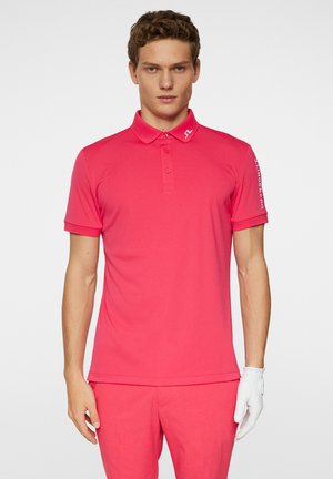 Polo rose avec un col, des manches courtes et une patte de boutonnage. Présente un détail de logo sur l'épaule gauche. Texture lisse.