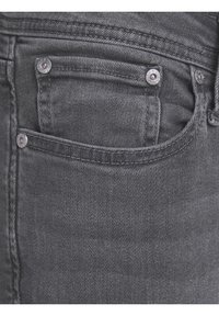 Jeans de mezclilla gris con un bolsillo para monedas, herrajes plateados y una textura suave con un ligero brillo. Costuras detalladas a lo largo de las costuras.