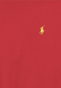 Röd tyg med en liten guldbroderad logotyp av en polo-spelare på en häst som håller i en klubba.