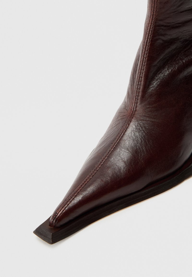 Donker bordeauxrode leren enkellaars met een puntige neus, een gladde textuur, subtiele stiksel details en een platte houten zool.