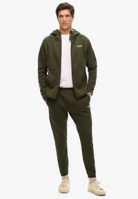 Set di felpa verde con cappuccio e pantaloni jogger in tessuto morbido. Felpa con cordini regolabili, zip completa e tasche laterali; pantaloni jogger con vita elastica.