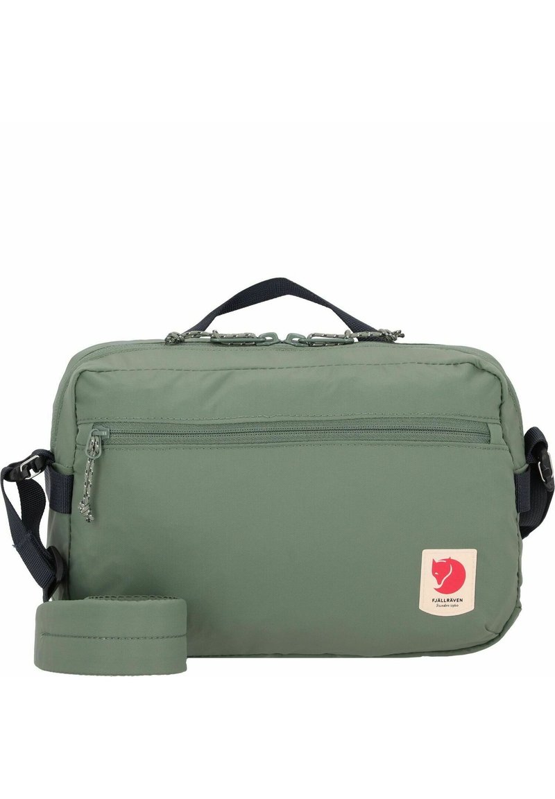 Green nylon bag with a rectangular shape, zippered main compartment, front pocket, and a logo patch. Adjustable strap included.