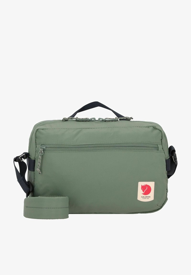 Green nylon bag with a rectangular shape, zippered main compartment, front pocket, and a logo patch. Adjustable strap included.