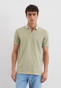 Polo shirt in lichtgroene katoen met korte mouwen, drie knopenlijst en klein logo op de linkerborst. Gecombineerd met blauwe jeans.