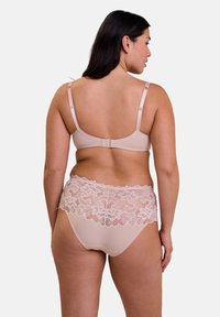 Set di lingerie in pizzo beige realizzato con un tessuto morbido e liscio. Il reggiseno presenta spalline regolabili, mentre la parte inferiore ha un design in pizzo floreale in vita.