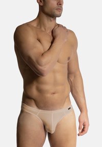 Béžové pánské trenýrky vyrobené z průhledné tkaniny, s nízkým pasem a jemnými švy, které zvýrazňují kontury těla.
