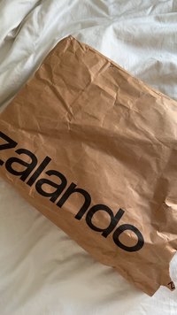 Bruin gekreukeld papieren verpakkingsmateriaal met een groot zwart "zalando"-logo, geplaatst op een wit stoffen oppervlak.