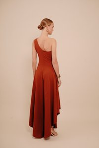 Aszimmetrikus, egyrészes ruha mély rozsda színben, testhezálló felsőrész cipzáras zárral, lebegő szoknya, sima textúra és elegánsan omló szegély.