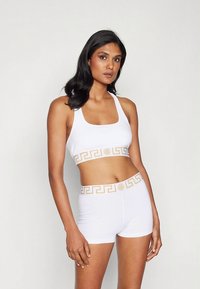 Baltas sportinis trumpas viršus ir šortai su auksiniu graikų rakto raštu juosmens diržo srityje. Lygi, prigludusi medžiaga be siūlių.