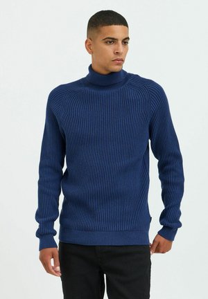 Navy ribbed turtleneck sweater made of textured knit fabric, featuring long sleeves and a fitted silhouette. Complemented by a subtle hem accent.