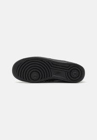 Black sneaker outsole featuring circular patterns, textured rubber, and a flat profile with pronounced treads for traction.