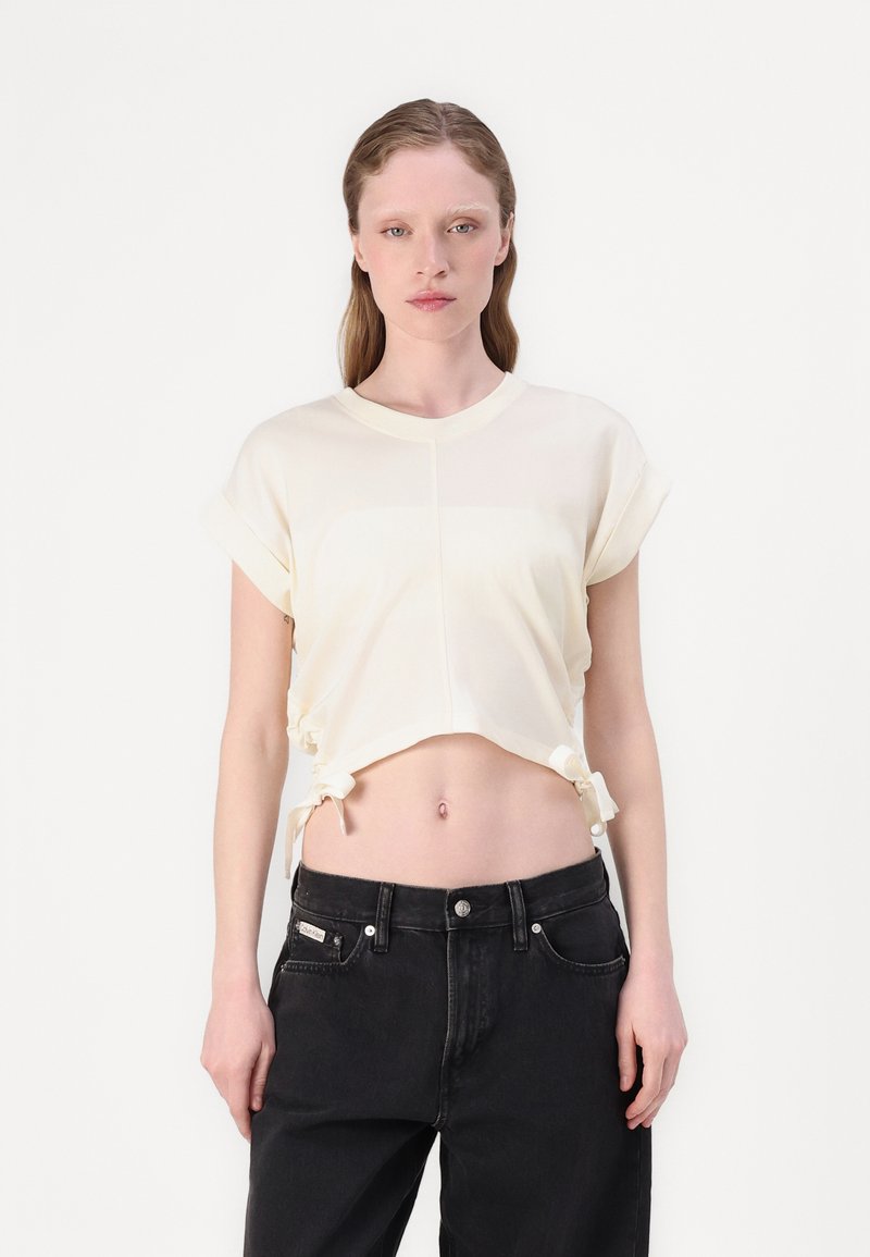 T-shirt cropped crema con maniche corte arrotolate, caratterizzato da lacci regolabili all'orlo. Abbinato a jeans neri a vita alta.