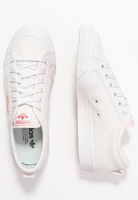 Vita Adidas kanvas-snörskor med vita snören, röd logotyp på tungan och hälen, visade från ovan och sidan mot en vit bakgrund.