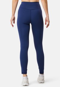 Marinblå leggings med hög midja, slät textur och smalnande ben, med en diskret logotyp på baksidan. Matchad med vita skor.