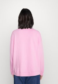 Ljusrosa sweatshirt med en avslappnad passform, rund halsringning och långa ärmar, med en mjuk textur. Synlig sömnad vid fåll och ärmslut.