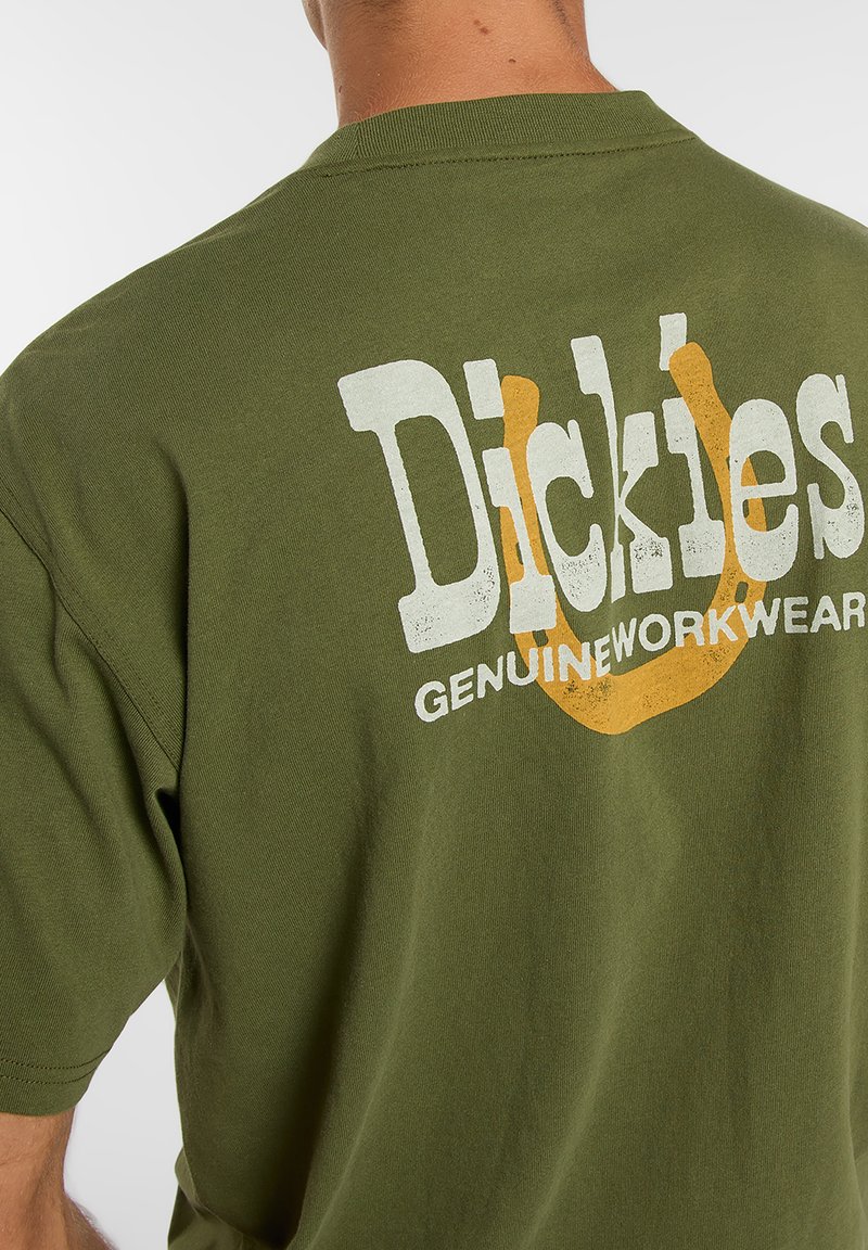 T-shirt en coton vert olive avec un grand logo blanc et orange au dos, portant les inscriptions "Dickies" et "Genuine Workwear".