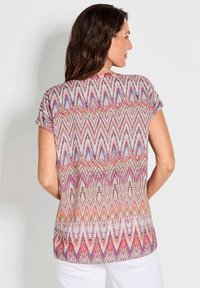 Kurzärmlige Bluse mit einem lebhaften, mehrfarbigen Chevron-Muster und feinen Details in rosa, blau und weißen Farbtönen.