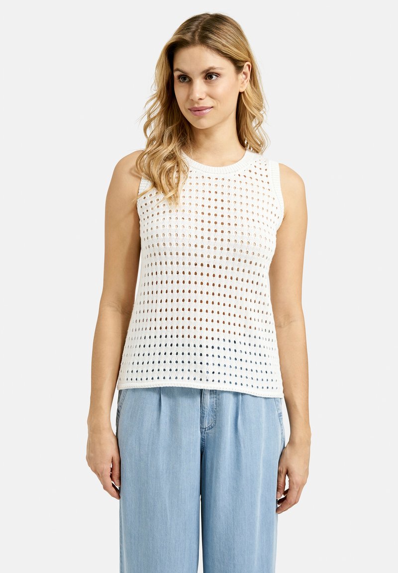 Weißes ärmelloses Stricktop mit einem strukturierten offenen Gewebe und kreisförmigen Mustern. Kombiniert mit hellblauen, locker sitzenden Hosen.