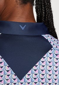 Collared shirt featuring a textured navy fabric with a geometric pattern in pink, blue, and green. Accented with a logo near the collar.