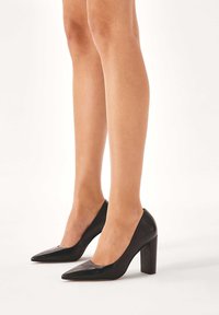 Scarpe con tacco alto in pelle nera, con punta affusolata e tacco a blocco, caratterizzate da una texture liscia e un design a vamp basso.