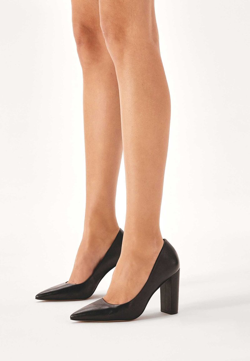 Scarpe con tacco alto in pelle nera, con punta affusolata e tacco a blocco, caratterizzate da una texture liscia e un design a vamp basso.
