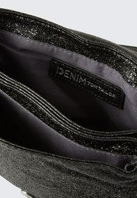 Schwarze Denim-Tasche mit glänzender Textur. Das Innere hat eine dunkle Fütterung und ein Etikett mit der Aufschrift "DENIM TOM TAILOR". Mehrere sichtbare Fächer.