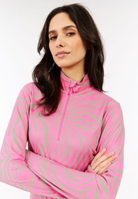 Top de manga larga con cremallera en un brillante color rosa, con rayas de cebra grises. Hecho de una tela elástica y suave. Presenta un cuello simulado y un diseño ajustado.
