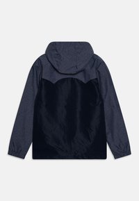 Námořnická modrá bunda s kapucí, která má texturovanou horní část, elastické manžety a hladkou, lesklou dolní část s kontrastním vzorem.