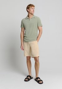 Lichtgroene polo met korte mouwen, gecombineerd met beige shorts. Zwarte sandalen met gesps Accenten maken de outfit compleet. Eenvoudig, casual ontwerp.