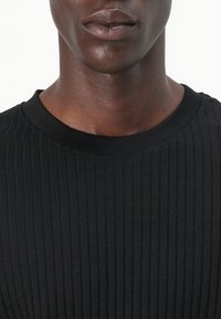 T-shirt noir en maille côtelée avec un col rond. Présente des lignes verticales texturées et est fabriqué à partir d'un tissu doux et extensible.