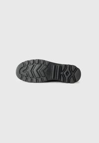 Black rubber shoe outsole with a textured, patterned design featuring deep grooves and ridges for traction. Solid construction and durable material.
