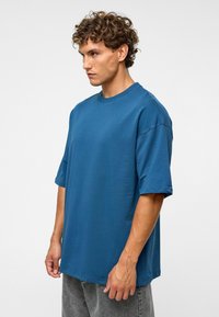 Teal oversized t-shirt van zachte katoenen stof, met een ronde hals, korte mouwen en een ontspannen pasvorm. Geen zichtbare patronen of accenten.