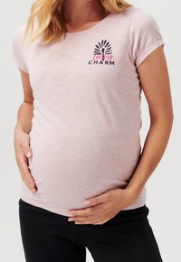 Světle růžové těhotenské tričko s krátkým rukávem a kulatým výstřihem. Disponuje grafikou "Lucky Charm" v černé a růžové barvě. Měkký, elastický materiál.