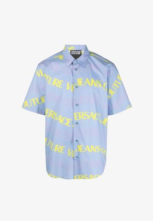 Camicia a maniche corte con bottoni in tessuto azzurro chiaro, con il testo audace giallo "VERSACE JEANS COUTURE" in varie orientazioni.
