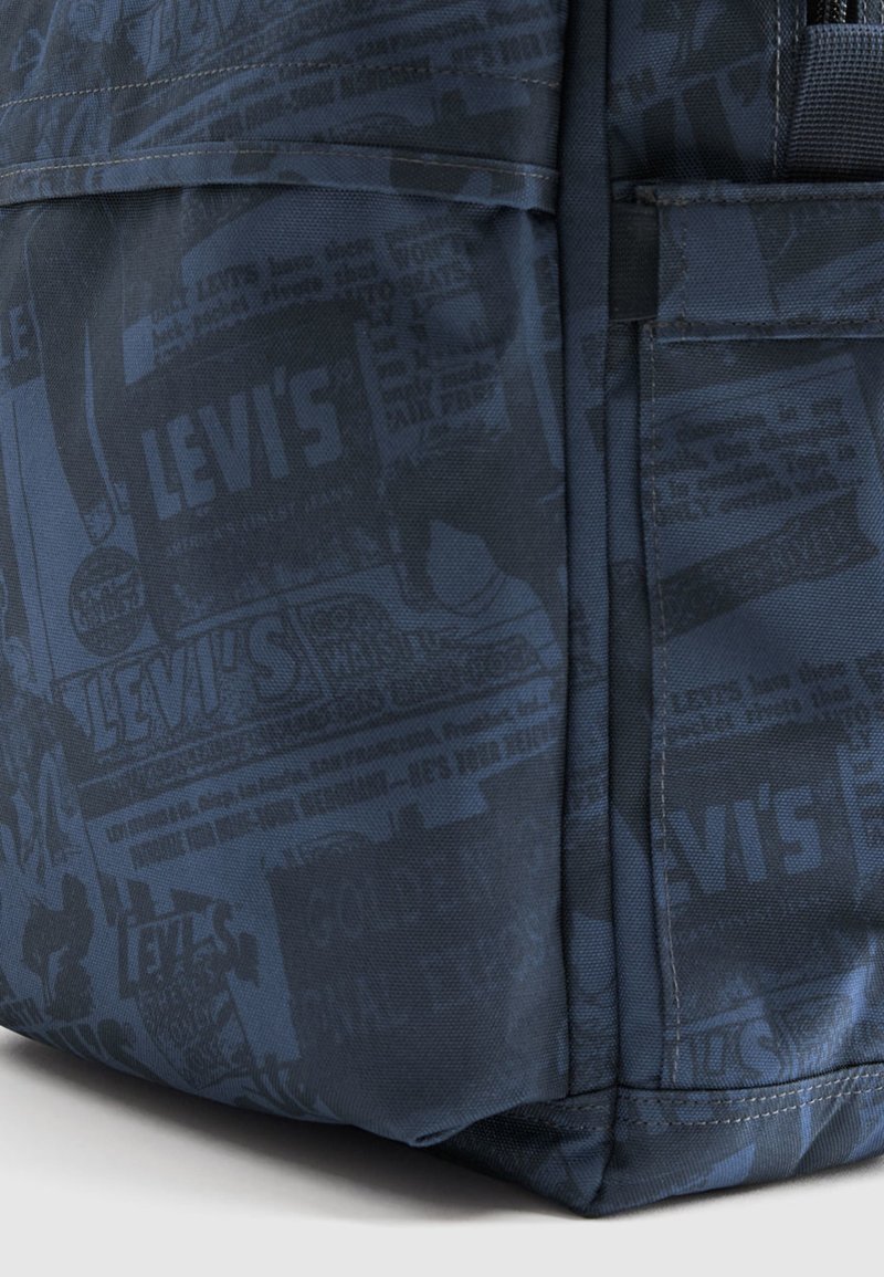 Mochila de tela azul con superficie texturizada y un estampado completo de logotipos y anuncios de la marca Levi's en un tono más oscuro.