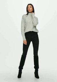 Pulôver de gola alta cinza com texturas caneladas, suave ao toque, combinado com jeans pretos justos e botas pretas até ao joelho. Design simples, sem padrões visíveis.