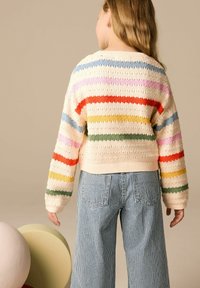 Pull en tricot court avec des rayures horizontales multicolores sur fond crème. Associé à un pantalon large à rayures bleues ; textures lisses et motif tricoté.