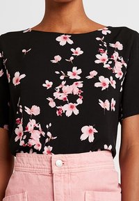 Svart kortärmad topp med rosa och vita blommor, bärs inknäppt i högmidjade ljusrosa byxor.