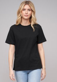 Schwarzes Baumwoll-T-Shirt mit Rundhalsausschnitt und kurzen Ärmeln. Bietet eine lockere Passform und eine glatte Textur, kombiniert mit hellblauen Jeans.