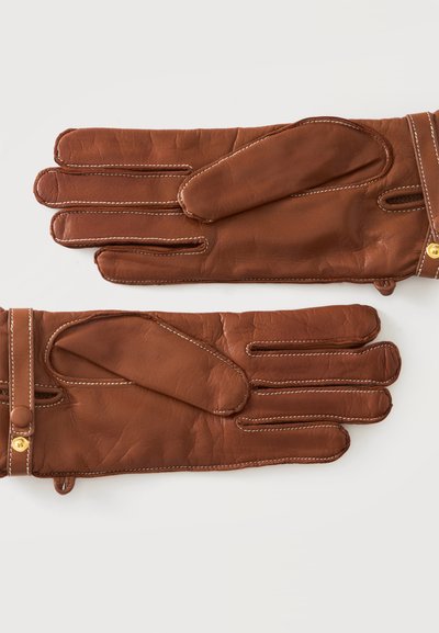 Paire de gants en cuir marron avec couture blanche et brides de poignet boutonnées sur un fond uni clair.