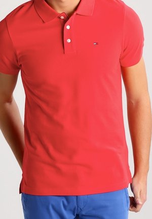 Camiseta polo roja de tela de algodón con cuello clásico, tapeta de tres botones y un pequeño logo en el pecho izquierdo. Mangas cortas, diseño ajustado.