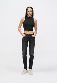 Čierny krátený top bez rukávov v páre s tmavými džínami, ktoré majú úzky strih a minimálne detaily. Biele tenisky dokončujú vzhľad.